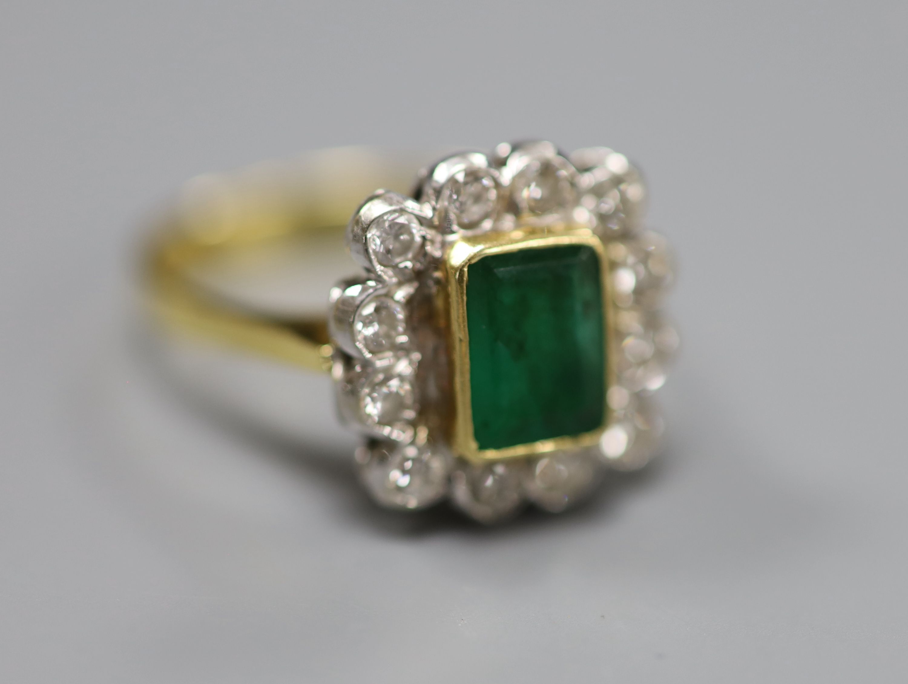 An emerald and diamond cluster ring, white and yellow metal setting (tests as 18ct), size Q, gross 6g.